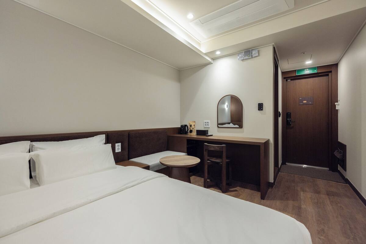 Una habitación de hotel con una cama, un escritorio, una silla, una mesa redonda y un espejo.