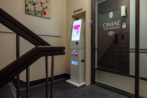 Entrada de un hotel con un quiosco de registro digital, una escalera y una puerta con la leyenda 'ONJAE STAY SEONGSU'.