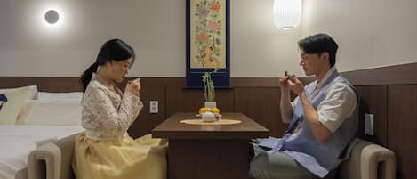 A room with a bed, a small table with a vase and a teapot, and a decorative painting on the wall.