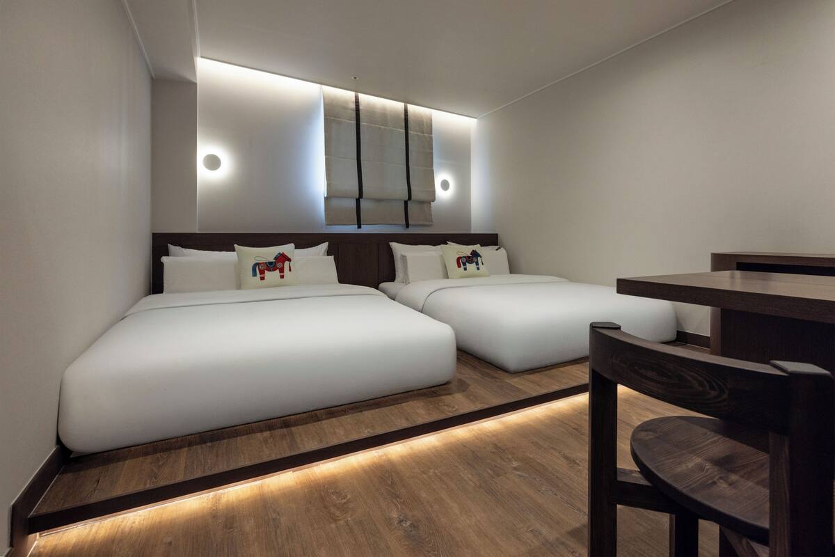 Habitación de hotel con dos camas, piso de madera, escritorio y ventana con persianas.