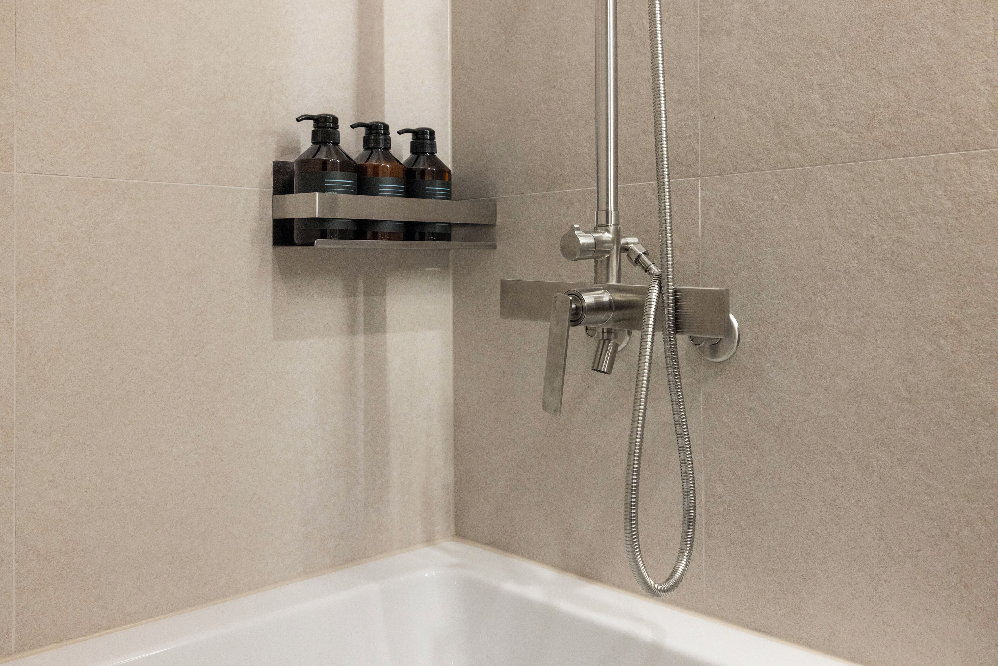 A shower area with a handheld showerhead, a wall-mounted faucet, and a shelf with toiletries.