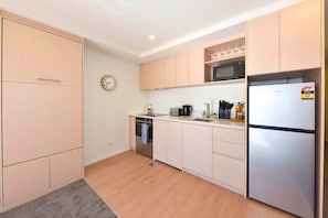 Een moderne keuken met lichte houten kastjes, een roestvrijstalen koelkast, een magnetron, een broodrooster en een klok aan de muur.