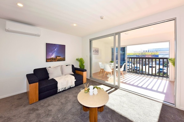 Ein modernes Wohnzimmer mit einer Couch, einem Couchtisch und einem Balkon mit Blick auf einen Parkplatz.