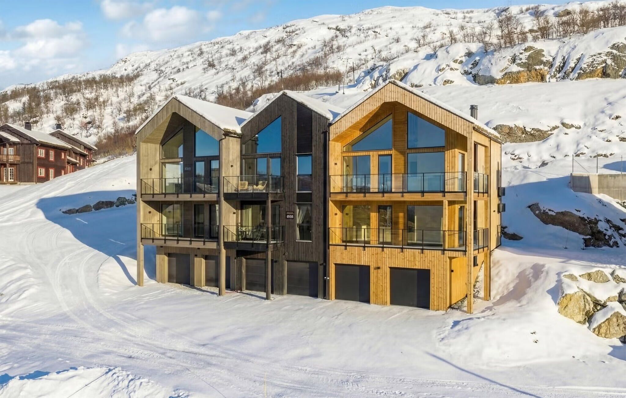 Un edificio moderno de madera con varios balcones y ventanas amplias, ubicado en una zona montañosa nevada.