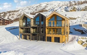 A modern wooden building with multiple balconies and large windows, situated in a snowy mountainous area.