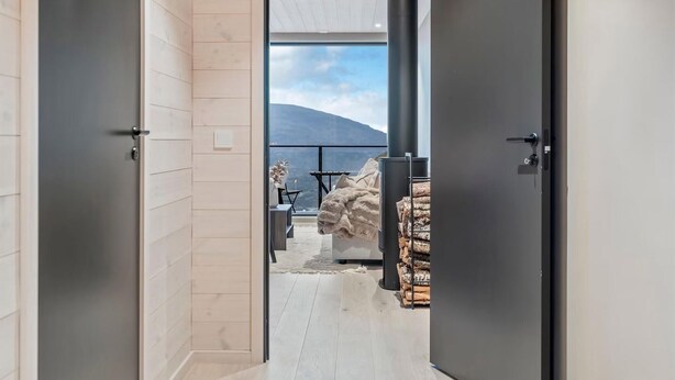 Ein modernes Interieur mit Holzboden, einer schwarzen Tür, einem Balkon mit Bergblick und einem Kamin mit Holz.