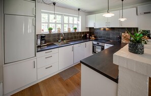 A modern kitchen with white cabinets, a black countertop, a built-in oven, and a window with potted plants. - Lovely home in Blåvand with WiFi (Blåvand)