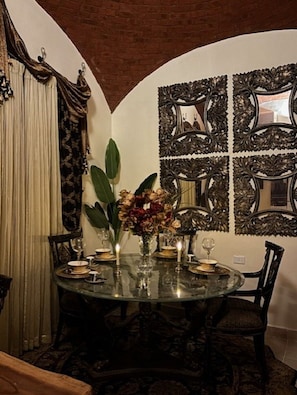 Zona pranzo con tavolo in vetro, sedie, un vaso con fiori e specchi decorativi alle pareti.