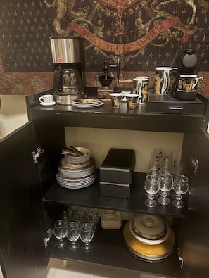 Angolo bar con una macchina per caffè, piatti impilati, bicchieri e un arazzo decorativo.