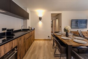 Eine moderne Küche mit einer Holzinsel, einem Essbereich mit einem langen Tisch, gedeckt für vier Personen, und einem Wohnbereich mit einer Couch und einem an der Wand montierten Fernseher.