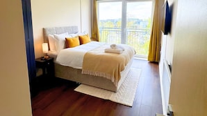 A hotel room with a bed, bedside table, lamp, and a view of the city through the window. - Spacious 2BR Feltham Home Sleeps 5 (Feltham)