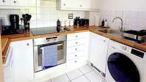 A compact kitchen with white cabinets, a built-in oven, a microwave, a sink, and a washing machine. - Spacious 2BR Feltham Home Sleeps 5 (Feltham)