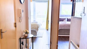 A hallway leading to two bedrooms with a 'Welcome Home' sign, a clock, a phone, and a small table with a vase. - Spacious 2BR Feltham Home Sleeps 5 (Feltham)