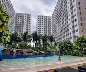 A swimming pool with a slide, surrounded by tall residential buildings and palm trees. - Comfystay Manila (Pasay City)