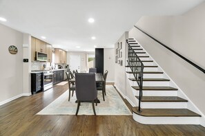 Une cuisine moderne avec des meubles en bois foncé, un coin repas comprenant une table et des chaises, et un escalier doté d’une rampe noire.