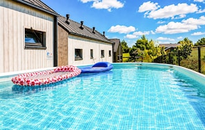 A swimming pool with two inflatable rings, a wooden building with windows, and a clear blue sky. - Awesome home in Kopan with heated swimming pool (Kopan)