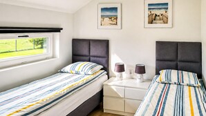 Habitación doble con dos camas, una ventana, una mesita de noche con lámparas y dos cuadros en la pared.