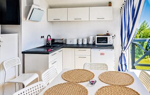 A compact kitchenette with a microwave, kettle, and storage containers. There are white chairs and a table with woven placemats. - Awesome home in Kopan with heated swimming pool (Kopan)