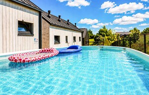 Ein Schwimmbecken mit zwei aufblasbaren Ringen, ein Gebäude aus Holz mit Fenstern und ein klarer, blauer Himmel.