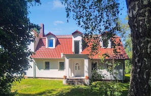 Une maison à deux étages, avec un toit recouvert de tuiles rouges, un petit porche à l’avant et une pelouse bien entretenue.