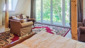 Ein Zimmer mit einer Couch, einem kleinen Tisch, einem großen Fenster mit Blick auf Bäume und einem gemusterten Teppich.