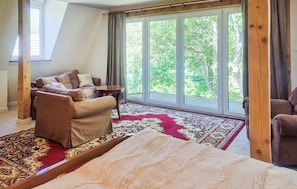 A room with a sofa, a small table, a large window with a view of trees, and a patterned rug.