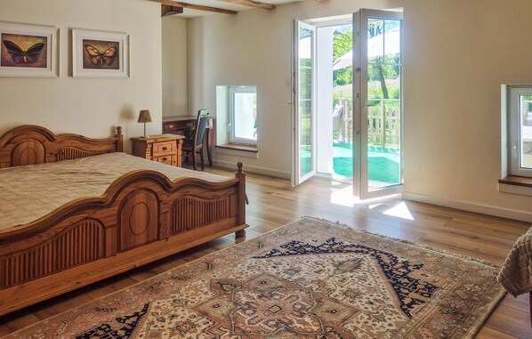A bedroom with a wooden bed, a desk, a chair, and a large window.
