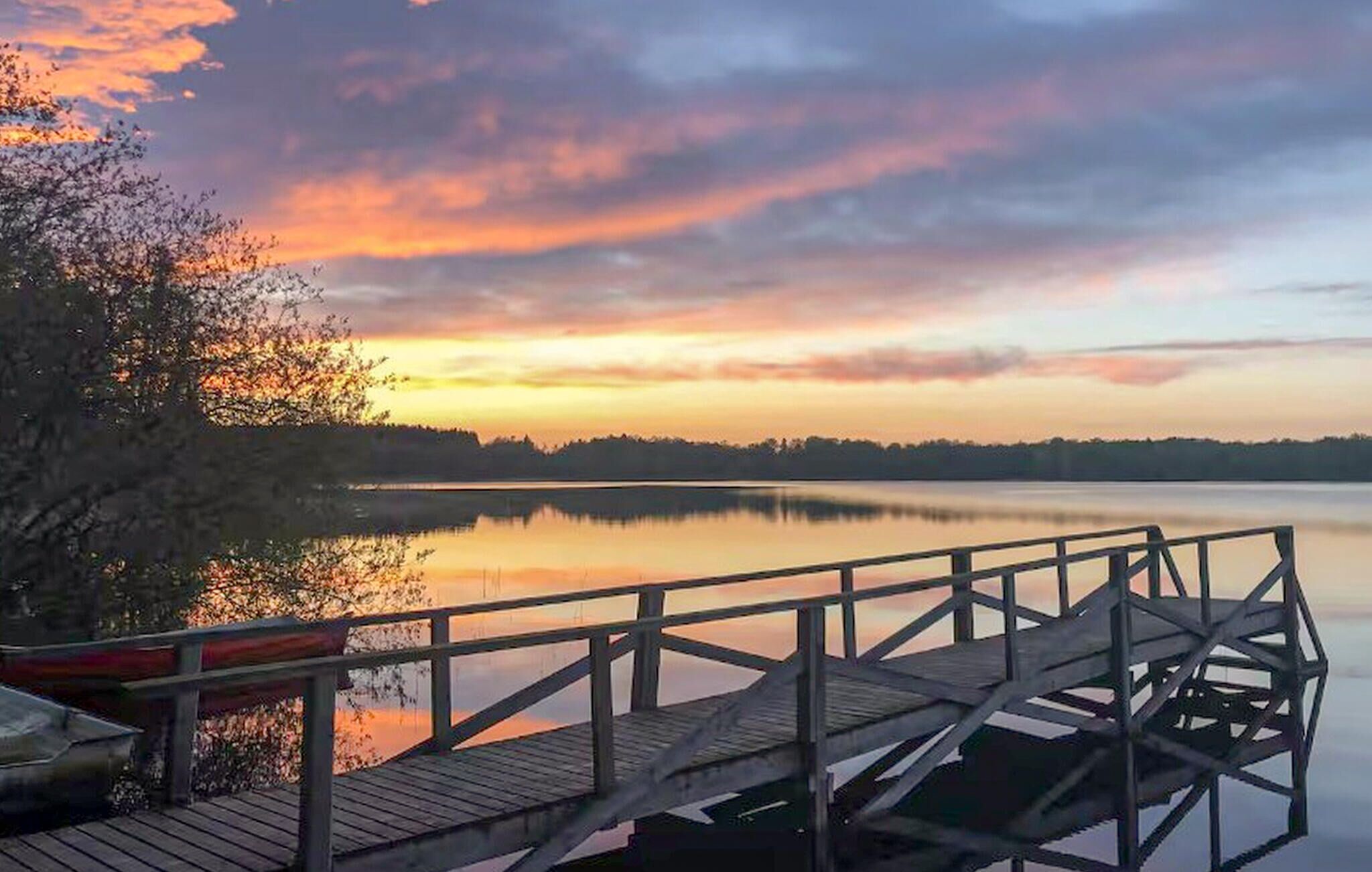 Une jetée en bois s’étendant sur un lac paisible, avec un coucher de soleil en arrière-plan.