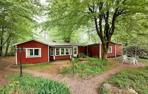 Ein rotes Holzhäuschen mit Schornstein, einer Veranda und einem Garten mit einer Bank.