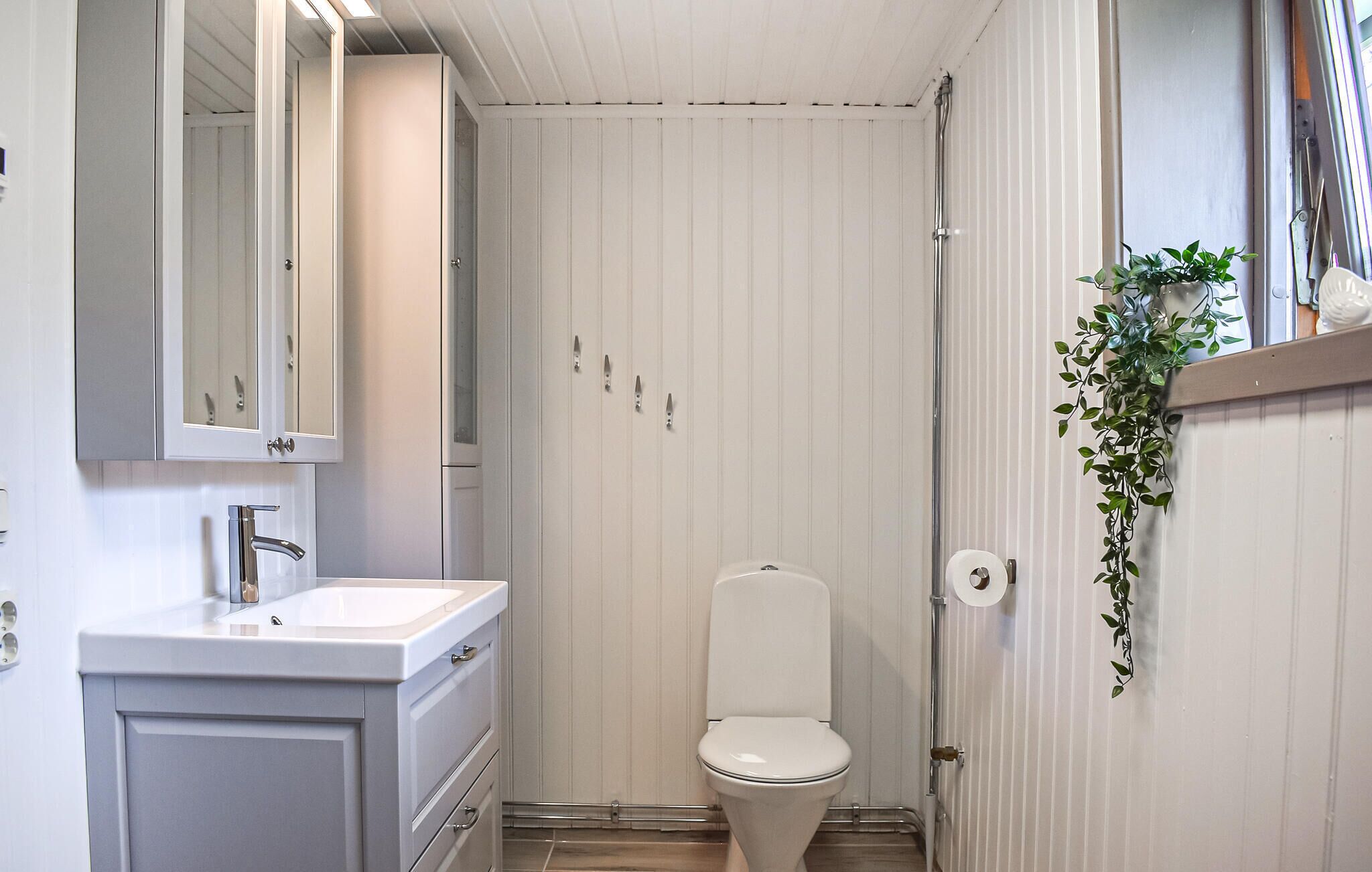 A bathroom with a toilet, sink, mirror, and a plant.