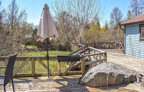 Eine Holzterrasse mit einem Metallstuhl, einem großen Felsen und einem überdachten Bereich mit Sonnenschirm.