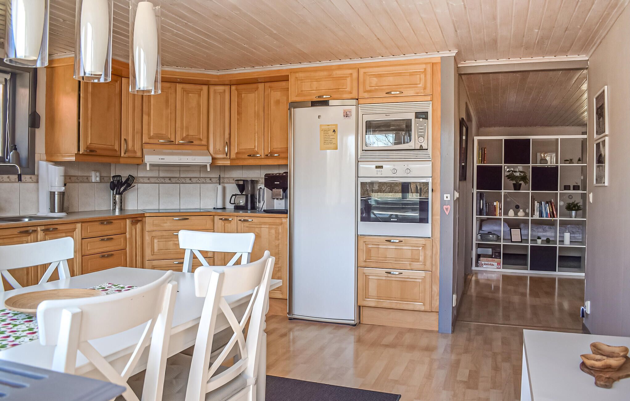 Una cucina con mobili in legno, un frigorifero, un forno e un'area pranzo con sedie bianche e un tavolo.