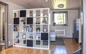 Ein Zimmer mit einer weißen Bücherwand, die mit Büchern und Dekoration gefüllt ist, einem Fenster mit Blick auf Bäume und einer eingebauten Klimaanlage.