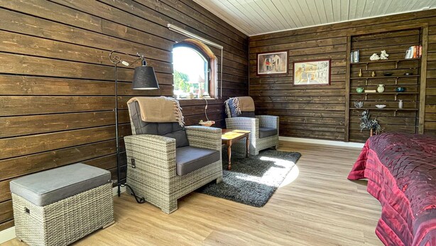 A cozy room with wooden walls, wicker furniture, a small table, and a bookshelf. - Awesome home in Reftele with WiFi (Reftele)