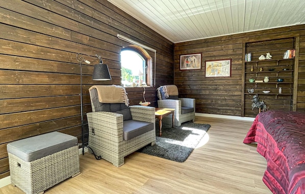 A cozy room with wooden walls, wicker furniture, a small table, and a bookshelf. - Awesome home in Reftele with WiFi (Reftele)