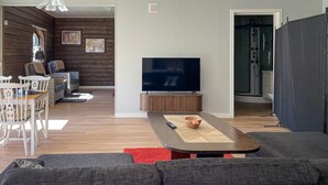A living room with a TV, wooden panel walls, a dining area with chairs, a sofa, and a red rug. - Awesome home in Reftele with WiFi (Reftele)