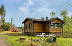A wooden cabin with a chimney, a small patio with a table and chairs, and a surrounding grassy area. - 3 bedroom beautiful home in Sjötofta (Sjötofta)
