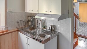 Une cuisine compacte équipée d’une cuisinière intégrée, d’un évier et d’un petit placard au-dessus du plan de travail.