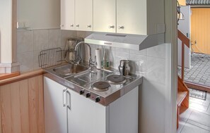 A compact kitchen with a built-in stove, a sink, and a small cabinet above the counter.