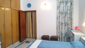 A bedroom with a bed, wooden wardrobe, a wall clock, a bedside table with a lamp, and patterned curtains. - Fabulous 2-bedroom bungalow with AC in charming Lucknow Gomtinagar (Lucknow)
