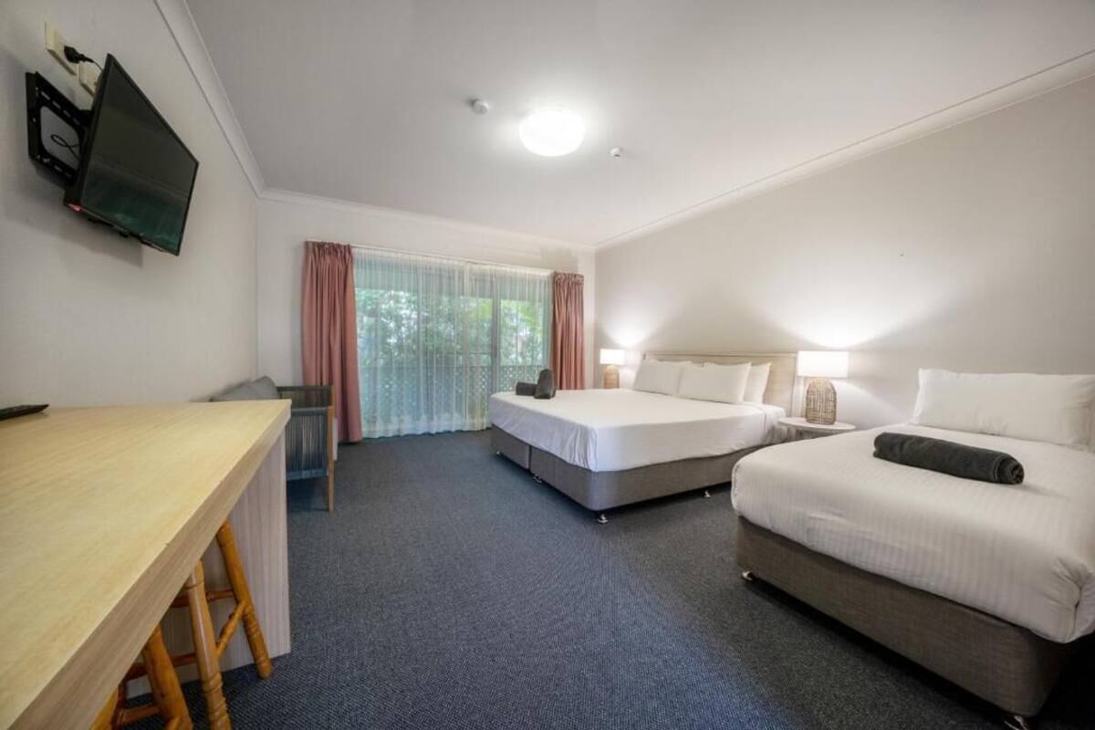 A hotel room with two beds, a desk, a television, and a window with curtains.