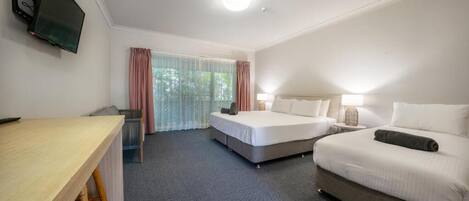 A hotel room with two beds, a desk, a television, and a window with curtains.