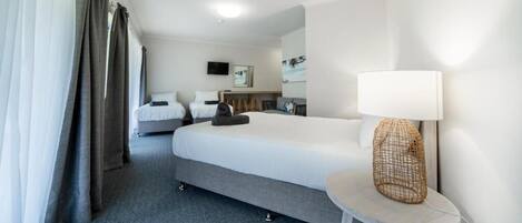 A hotel room with a large bed, a bedside table with a lamp, a small table with a chair, and a television on the wall.