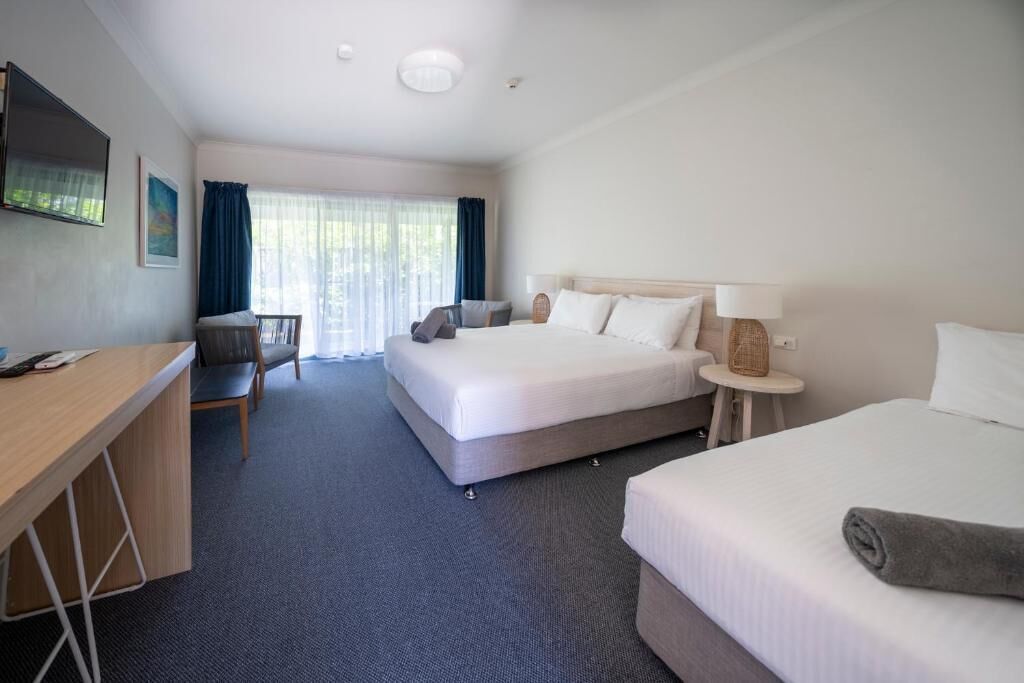 A hotel room with a bed, a desk, a chair, and a small table.