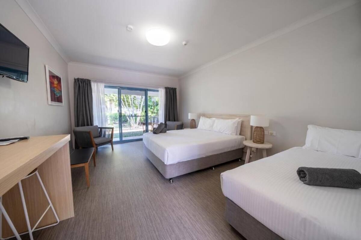A hotel room with a bed, a desk, a chair, a lamp, and a TV.