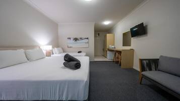 A hotel room with a bed, a sofa, a desk, a TV, and a painting on the wall.