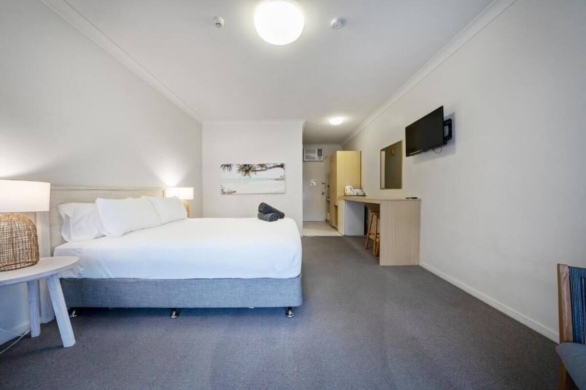 A bedroom with a bed, bedside table, lamp, TV, and a desk with a chair.