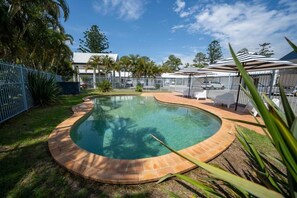 A swimming pool with a curved edge, surrounded by a fence and greenery. - Woolgoolga Coast Motel (Woolgoolga)