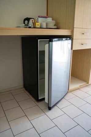 Un petit réfrigérateur dans une cuisine dotée d’un sol carrelé, d’un plan de travail en bois et d’un meuble de rangement en bois.
