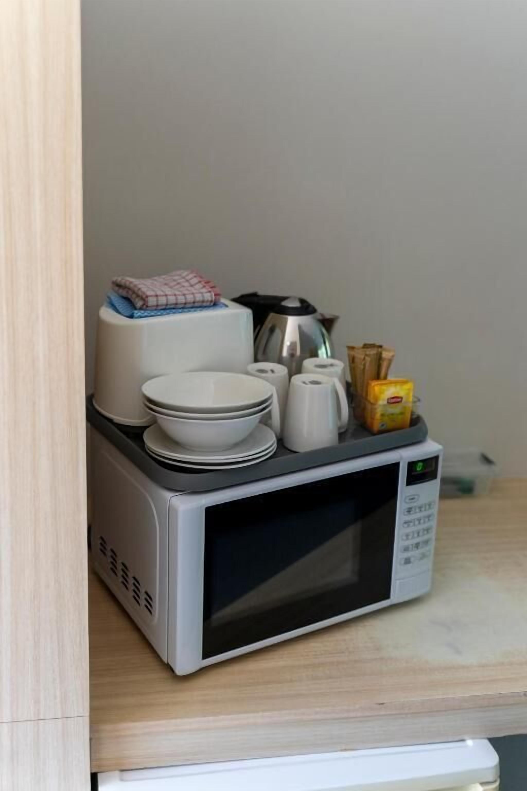 A microwave oven with a digital display, stacked white plates, a white kettle, and a small yellow box on a kitchen counter.
